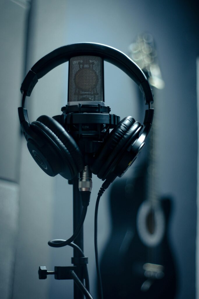 Close-up of microphone with headphones on stand in a dimly lit recording studio.